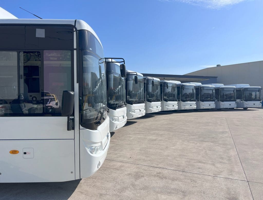 A row of white Battery Electric Buses (BEB) from Yutong lined up in an outdoor lot under a clear blue sky.